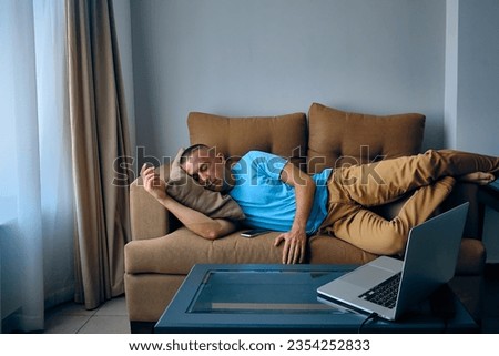 Young adult caucasian man felt asleep on a couch watching movies on laptop. Tired man sleeps on sofa Royalty-Free Stock Photo #2354252833