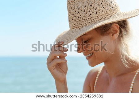 Woman radiates summer vibes wearing yellow striped bikini and a straw hat, enjoying her time on the sandy beach.