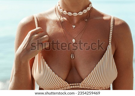Closeup of female neck with golden necklace with palm trees and seashells on a sunlit beach.