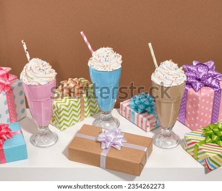 Image of beautiful milkshakes on table with colorful celebrate gifts, creamy tasty desserts. Birthday composition.