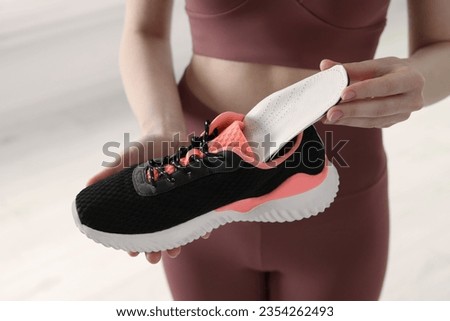 Sporty woman putting orthopedic insole into shoe on blurred background, closeup. Foot care Royalty-Free Stock Photo #2354262493