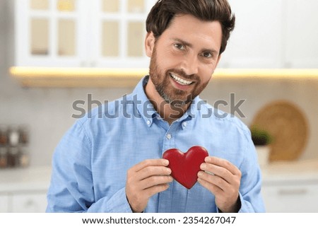 Happy bearded man holding red heart indoors