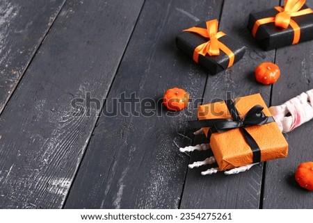 Skeleton hand with gift boxes and pumpkins for Halloween celebration on black wooden background