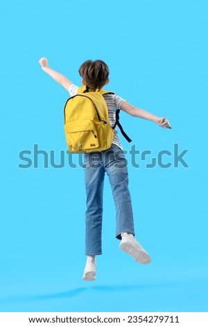 Jumping little boy with schoolbag on blue background, back view Royalty-Free Stock Photo #2354279711