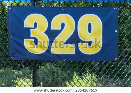 329 foot ft baseball field distance sign in yellow and black mounted on the black vinyl outfield fence.	