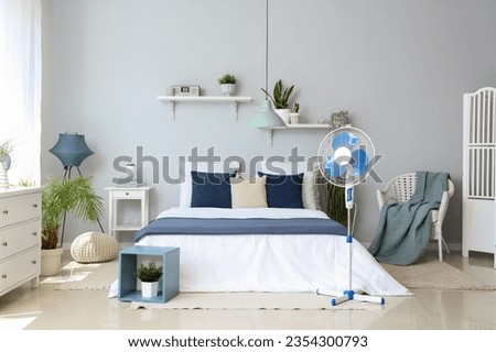 Interior of light bedroom with cozy bed and floor fan Royalty-Free Stock Photo #2354300793