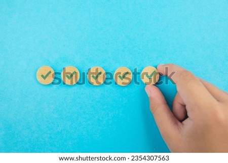 Checklist concept, check mark on wooden blocks, blue background with copy space. A hand holds wooden blocks with checkmarks.