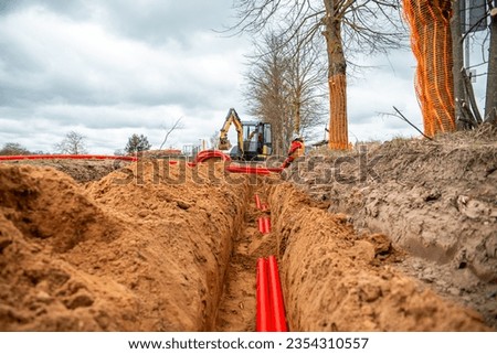 Network cables in red corrugated pipe are buried underground on the street. underground electric cable infrastructure installation.  Royalty-Free Stock Photo #2354310557