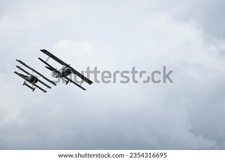 WW1 biplane and triplane fighter aircraft in simulated dogfight over airfield in Cambridgeshire, England on overcast day. Royalty-Free Stock Photo #2354316695