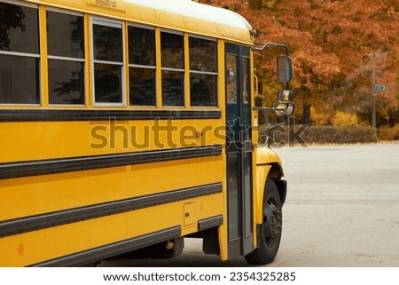 Yellow school bus stands in parking lot against the background of autumn park.