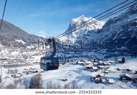 Winter scenery of Grindelwald village on the snowy hillside with Wetterhorn mountain under blue sky in background, viewed from a gondola of Eiger Express cableway, in Berner Oberland, Switzerland Royalty-Free Stock Photo #2354333335