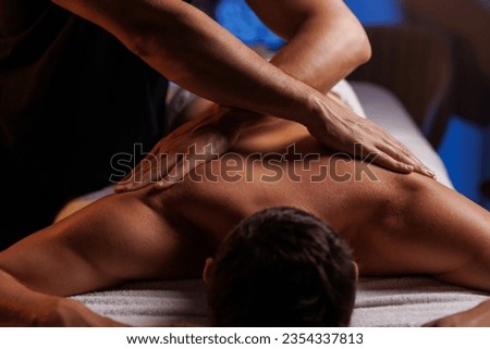 Physiotherapist massaging male patient with damaged shoulder muscle, treating sports injuries. Relaxing professional shoulder massage in cozy atmosphere, reboot on the weekend, end of difficult week. Royalty-Free Stock Photo #2354337813