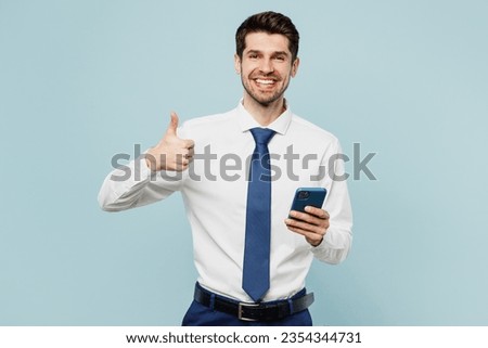 Young fun employee business man corporate lawyer wear classic formal shirt tie work in office hold in hand use mobile cell phone show thumb up isolated on plain pastel blue background studio portrait Royalty-Free Stock Photo #2354344731