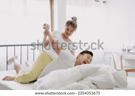 Funny asian couple wife giving husband hurt massage in white bedroom.