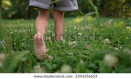 girl walks on the grass barefoot in the park. happy family kid dream concept. bare feet close-up walks on the grass in summer lifestyle child. daughter walks barefoot on the grass in the park