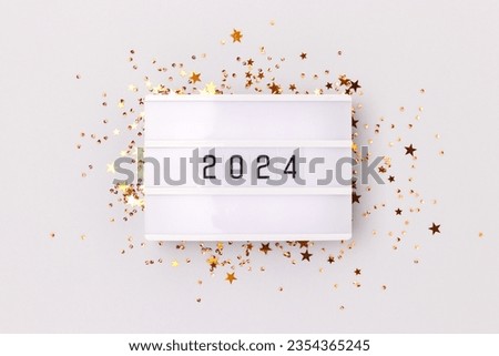 Lightbox with 2024 numbers and golden stars confetti on a gray background. New Year concept.