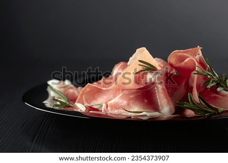 Italian prosciutto or Spanish jamon with rosemary on a black plate. Royalty-Free Stock Photo #2354373907