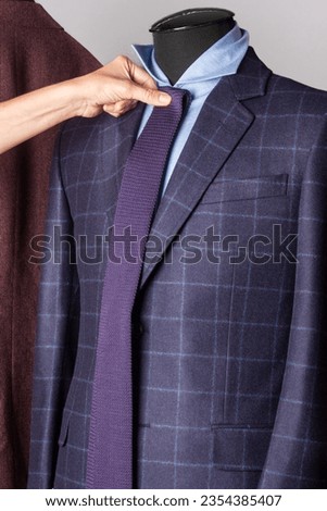 Suit with a tie. A woman's hand tries on a tie to a jacket and shirt on a mannequin. Shallow depth of field