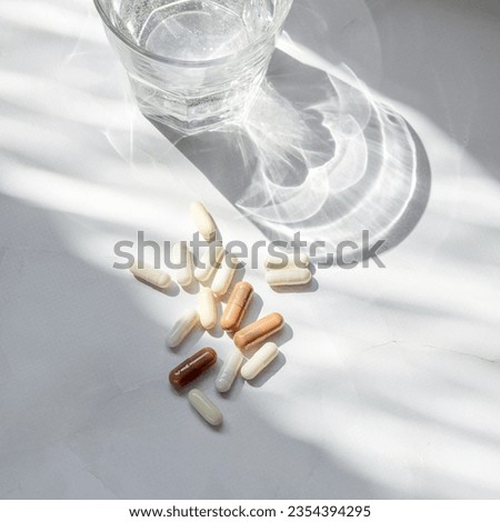 Minimal beauty, wellness, pharmaceutical industry concept. Different pills, capsules, glass with pure water on neutral white background with aesthetic sunlight shadow. Royalty-Free Stock Photo #2354394295