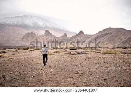 Back view of unrecognizable man tourist strolling on dry rocky terrain near mountainous area in cloudy day Royalty-Free Stock Photo #2354401897
