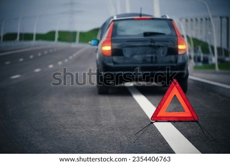 Red emergency stop sign on road. Blurred broken down car with warning signal. Warning triangle on roadside. Safe traffic, emergency situation in trip.