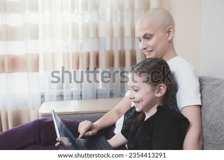 Sick woman with cancer spend time with her young child, looking at pictures on laptop. Family support concept.