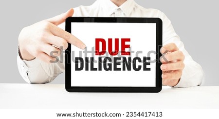 Text DUE DILIGENCE on tablet display in businessman hands on the white background. Business concept