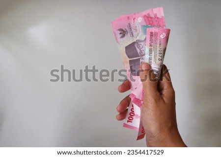Money in the hand (Hand with money, Hand holding Banknotes). IDR bank notes denomination one hundred thousand.