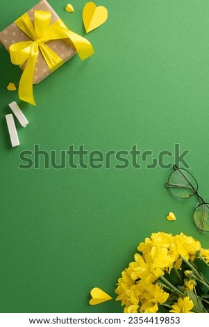Delve into Teacher's Day atmosphere with vertical top-view arrangement: yellow chrysanthemum bunch, giftbox, chalk, glasses, hearts. On green blackboard backdrop, find space for text incorporation