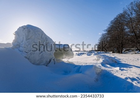 Winter landscape. Panoramic view of beautiful sunset on bay. Ice, snow and rocks on coastline. Setting sun in bright light. High quality photo