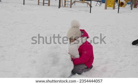happy kid girl and boy in red pink coat playing outdoor in snowy winter city. children play outside with snow during christmas holidays, make a snowman. Happy childhood and active winter holidays.
