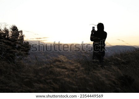 Woman taking pictures with her phone of a sunset in the mountains. Travel, technology and lifestyle concept.