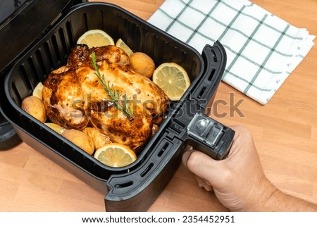 HAND COOKING WHOLE ROASTED CHICKEN WITH GARNISH IN AIR FRYER AT THE KITCHEN. TOP VIEW Royalty-Free Stock Photo #2354452951