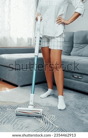 A young woman cleans the house with a vacuum cleaner. Upright vacuum cleaner cordless. Battery powered vacuum cleaner. Royalty-Free Stock Photo #2354462913