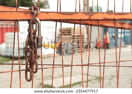 chain and pad key lock on orange locked gate for dirt yard parking lot with containers bins skids palettes, close up looking straight