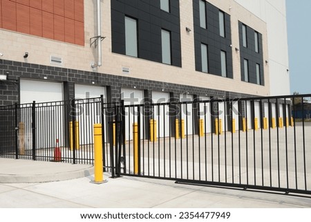 line row of exterior outdoors outside building public storage white garage units behind black metal fence mechanical gate on cement pavement Royalty-Free Stock Photo #2354477949