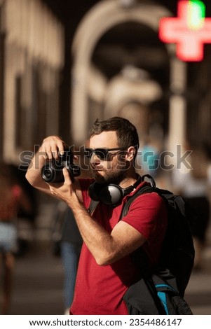 A young man, a traveler, taking pictures with a digital camera, on the street, in a city in Spain.