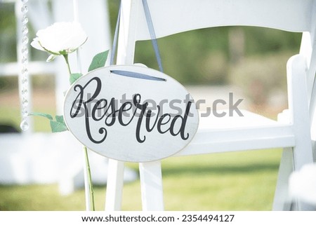 White round "reserved" wedding sign with black text hanging from chair at wedding ceremony isle