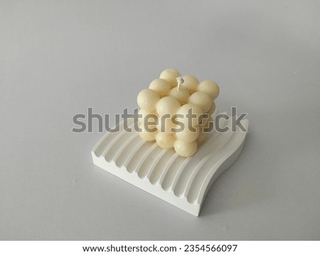A square scented candle is placed on a white stone slab. on a white background
