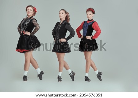 Dance performance. Irish ensemble of three beautiful women in concert costumes and Ghillies Hard Shoes dance together in a row. Full-length studio portrait on a grey background. Royalty-Free Stock Photo #2354576851