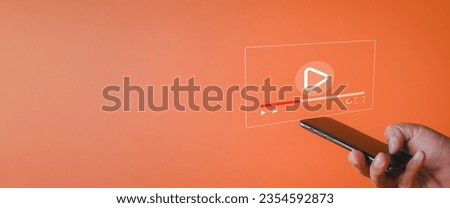 Live stream,Online live video,Online Marketing,e-learning,education,training,social media concept.,Hand holding smartphone with Multimedia video player icon over orange background with copyspace. Royalty-Free Stock Photo #2354592873