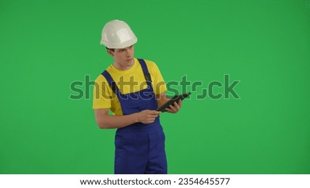 Medium green screen isolated chroma key shot of a young construction worker holding a tablet and looking around.