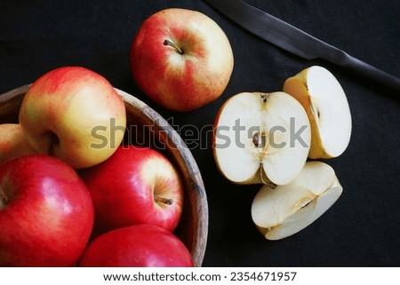 Sliced ​​apple next to other apples and knife on black background