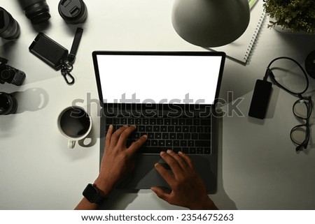 Above view of photographer using laptop on white table with digital camera, memory card and lens
