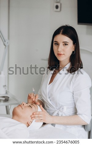 Portrait of charming woman in white bathrobe sitting on daybed and looking at beautician with smile while she touching her shoulder. High quality photo