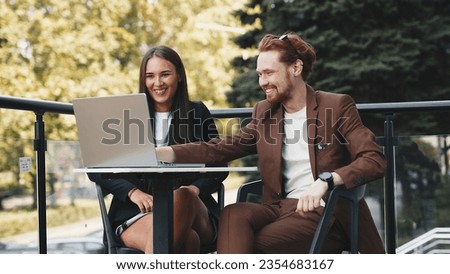 Portrait of a business woman and a businessman using a laptop together on a summer terrace. Business people are happy and celebrating the signing of an important contract.