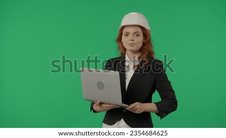 A woman architect in a protective helmet and with a laptop on a green screen background in the studio. Advertising area, workspace mock up.