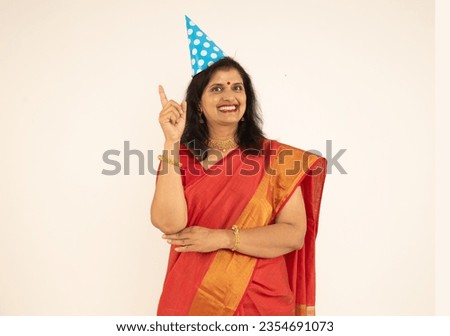 Portrait of Indian beautiful happy women wearing birthday cap. standing isolated over white background. wearing traditional colorful red saree in celebrating of birthday theme.
