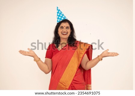 Portrait of Indian beautiful happy women wearing birthday cap. standing isolated over white background. wearing traditional colorful red saree in celebrating of birthday theme.