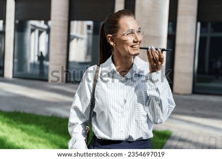 A person records a voice message, dictating words into a microphone. Financier female office employee uses the phone. A manager in modern office clothes. Royalty-Free Stock Photo #2354697019
